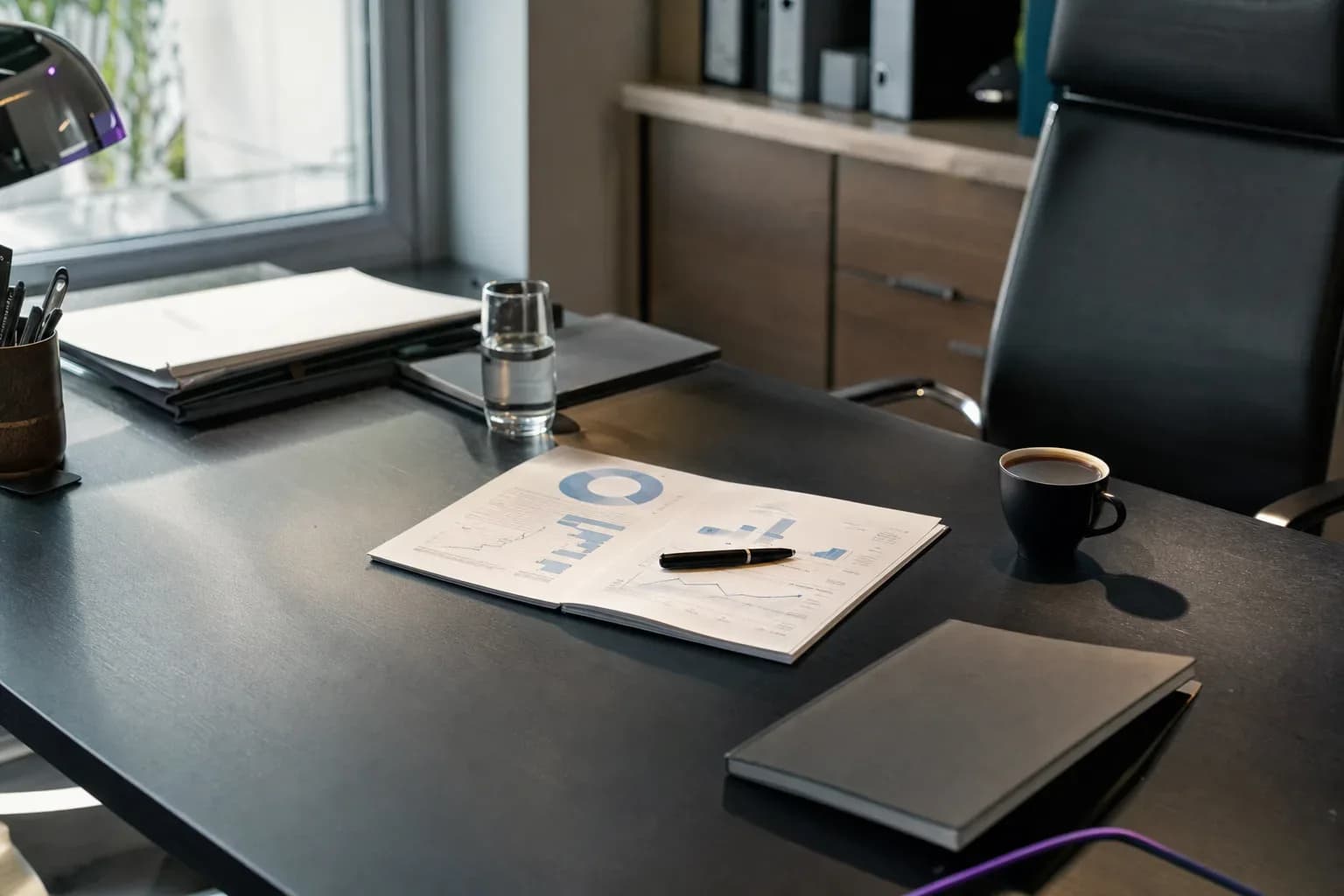Schreibtisch in einem Büro mit aufgeschlagenem Bericht voller Diagramme, Kugelschreiber, Kaffeetasse und Notizbuch